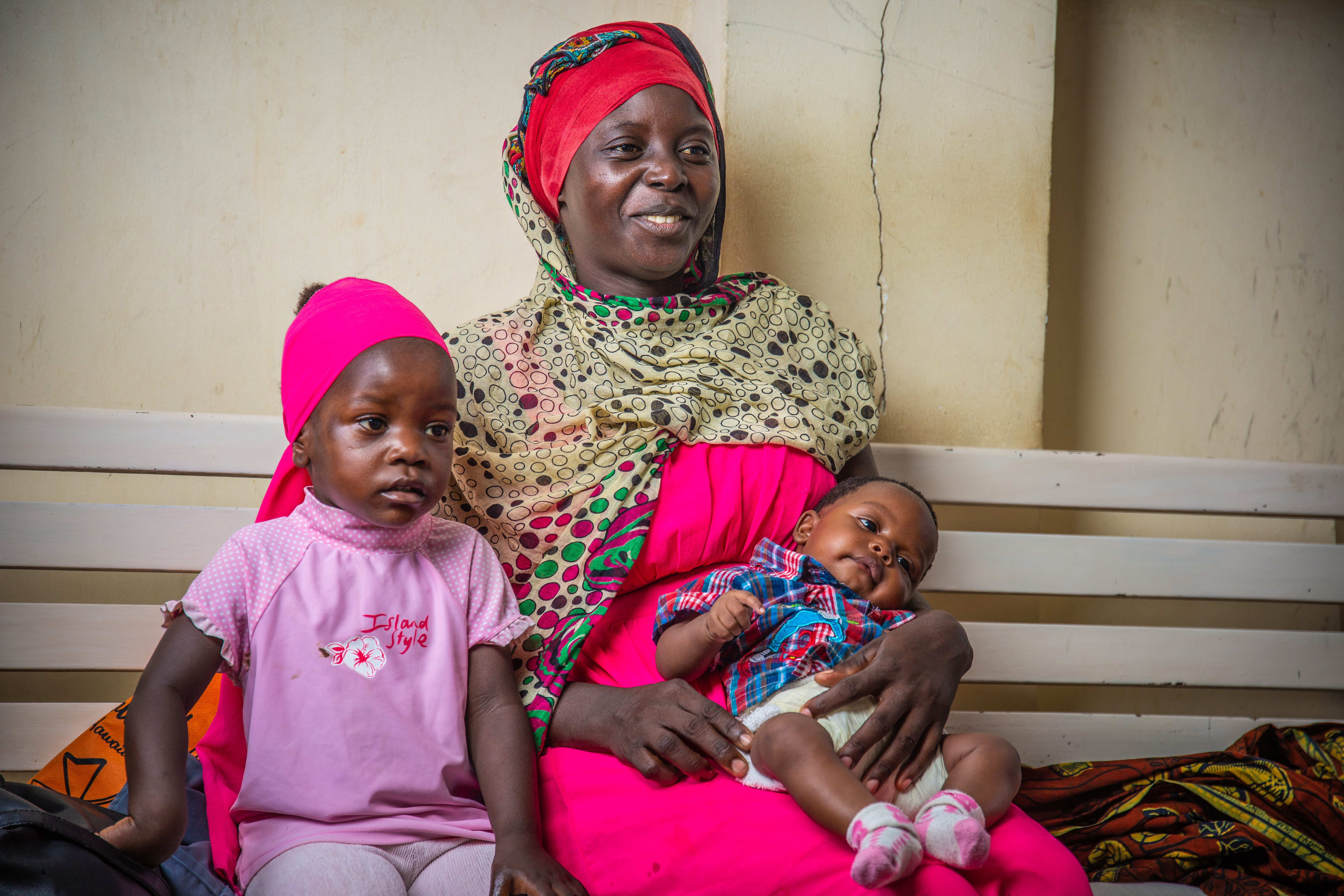 A happy mother sits with her two young children. One is an infant.