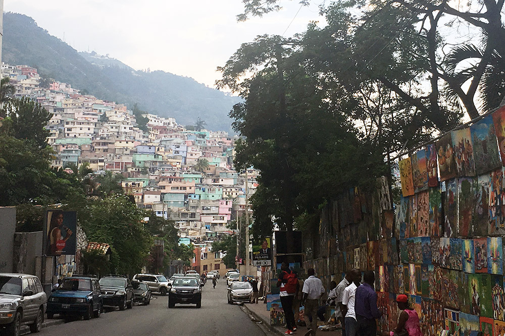 Picture of of a street in Port au Prince, Haiti with cars on the road and rows of houses on a hill in the background.