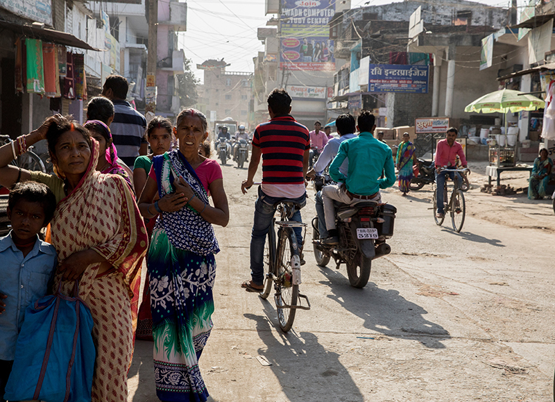 Photo of a busy street in India with people walking and riding bikes.