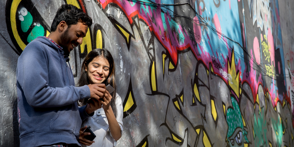 A man and a woman leaning against a wall covered in graffiti while looking at a phone