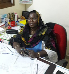 Ndieng sitting at a desk with a ledger book in front. 