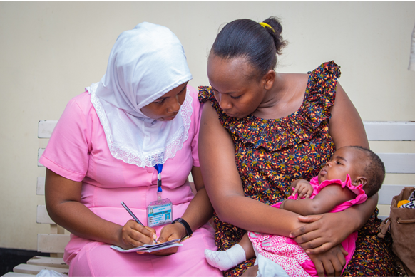 Nursing student wearing pink working with a mother and child.